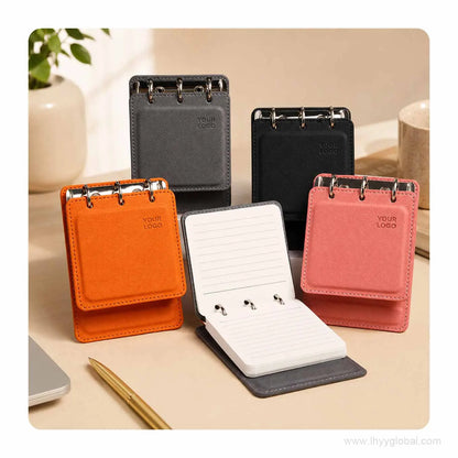 Custom logo pocket loose-leaf notebooks in Orange, Cherry Pink, Mist Gray and Black displayed on an office desk.