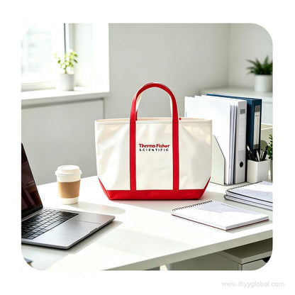 Executive office desk setup featuring a custom white and red tote bag placed among a laptop, coffee cup, and spiral notebooks for professional corporate branding.